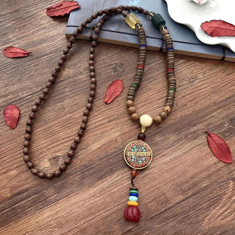 Tibetan mala necklace with coconut shell beads and mantra charm displayed on wooden surface with autumn leaves