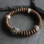 Brown coconut shell Om Mani Padme Hum bracelet with silver accents, overhead flat lay on dark slate background