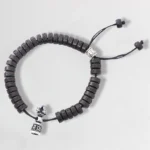 Tibetan coconut shell Om Mani Padme Hum prayer bracelet, top view featuring dark brown carved beads with silver vajra charm and adjustable black drawstring