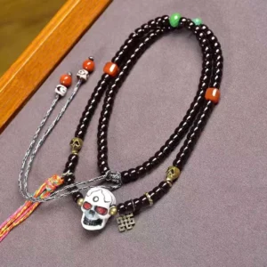 Tibetan coconut shell skull bracelet with colorful accent beads and brass charm, displayed flat lay on wooden surface