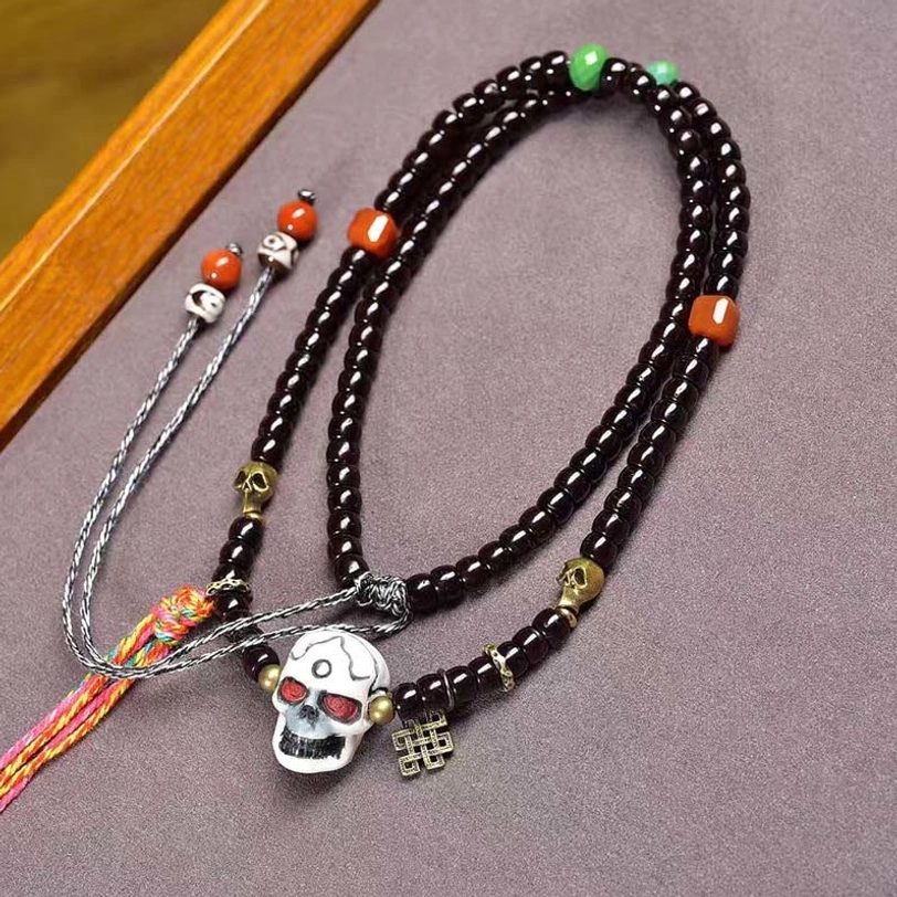 Tibetan coconut shell skull bracelet with colorful accent beads and brass charm, displayed flat lay on wooden surface