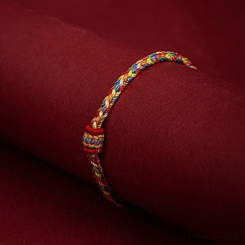 Handmade Tibetan protection bracelet being worn on wrist showing braided design and decorative knot detail on fabric background