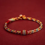Handmade Tibetan colorful protection bracelet with braided multicolor threads, decorative knot and metal clasp on dark red background