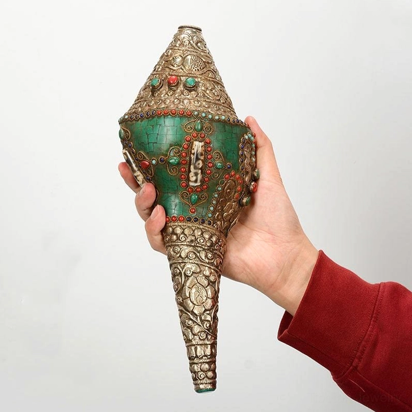 Tibetan conch shell ornament held in hand showing central inlaid panel with turquoise body and double dorje symbol, handheld view