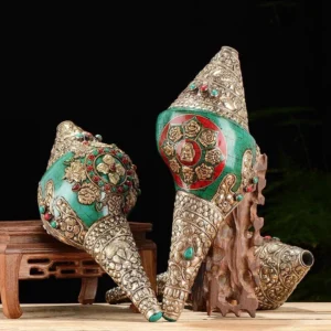 Two Tibetan decorated conch shell ornaments with carved silver patterns and Buddha mandala inlays on wooden display stands, comparison view
