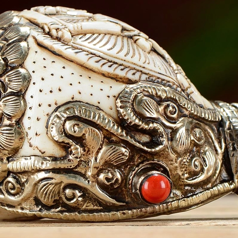 Detailed view of Tibetan conch silver filigree carving with floral patterns and red bead inlay