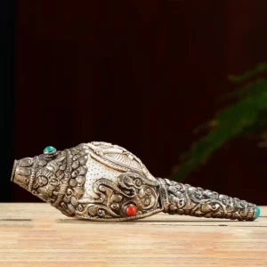 Tibetan engraved conch ornament featuring intricate silver scrollwork and buddhist relief design on wooden surface