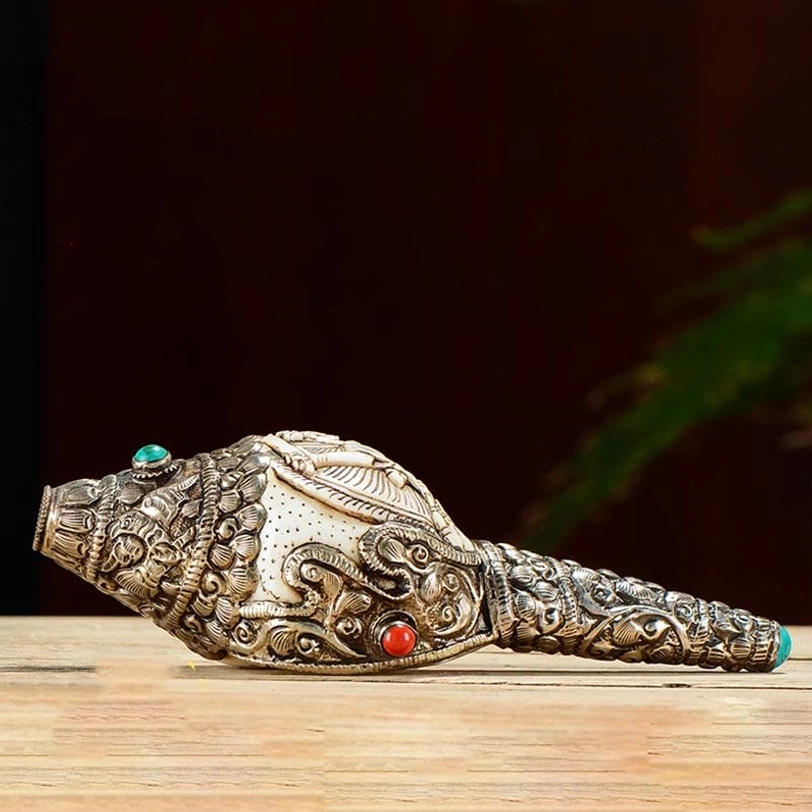 Tibetan engraved conch ornament featuring intricate silver scrollwork and buddhist relief design on wooden surface