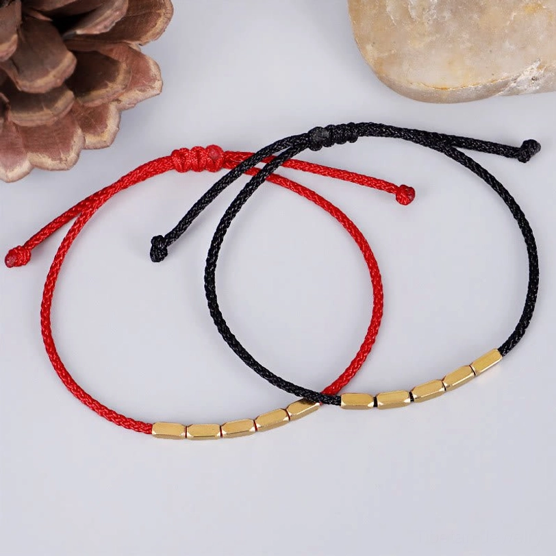 Matching pair of red and black Tibetan protection bracelets with copper beads, displayed with natural pine cone decoration
