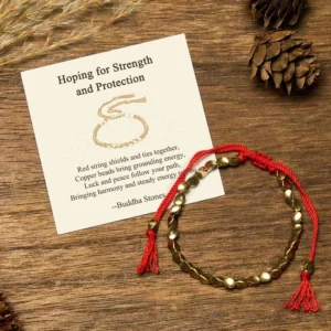 Tibetan copper beads protection bracelet with red braided cord, matte oval beads, and blessing message card on wooden surface with natural elements
