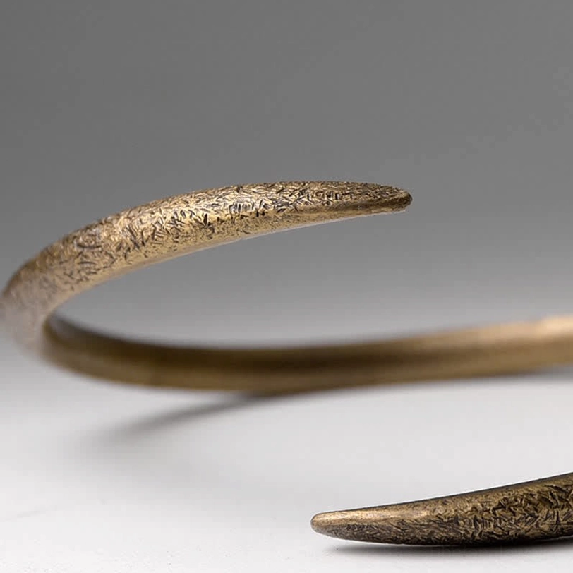 Close-up extreme detail of open copper claw cuff bracelet, matte textured surface, adjustable tapered claw ends, grey background