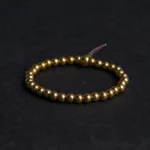 Tibetan copper brass bead bracelet flat lay with brown tassel on dark fabric background