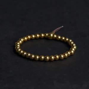 Tibetan copper brass bead bracelet flat lay with brown tassel on dark fabric background