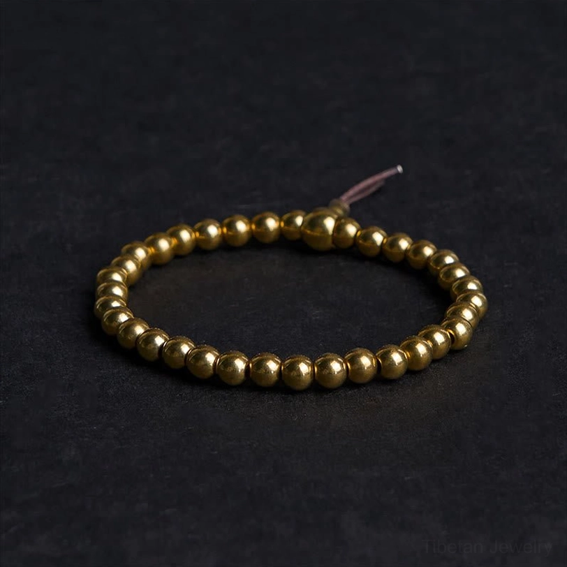 Tibetan copper brass bead bracelet flat lay with brown tassel on dark fabric background