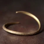 Tibetan copper claw cuff bracelet with open adjustable design, antique bronze-gold finish, flat lay on dark wooden surface