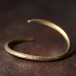 Tibetan copper claw cuff bracelet with open adjustable design, antique bronze-gold finish, flat lay on dark wooden surface