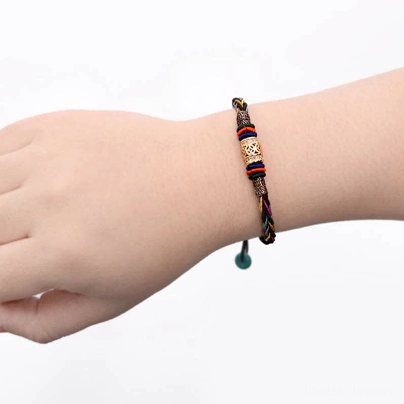 Tibetan red string protection bracelet worn on human wrist showing slim braided cord, engraved metal bead, and adjustable fit