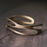 Tibetan copper cuff bracelet with layered hollow wave pattern, adjustable 55mm inner diameter, shown from three-quarter overhead angle on dark wooden surface