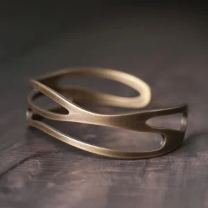 Tibetan copper cuff bracelet with layered hollow wave pattern, adjustable 55mm inner diameter, shown from three-quarter overhead angle on dark wooden surface