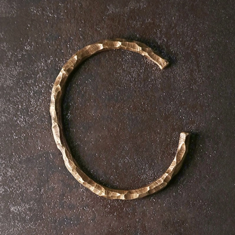Top-down view of Tibetan C-shaped open cuff bracelet showing hand-hammered bumpy texture in warm brass tone