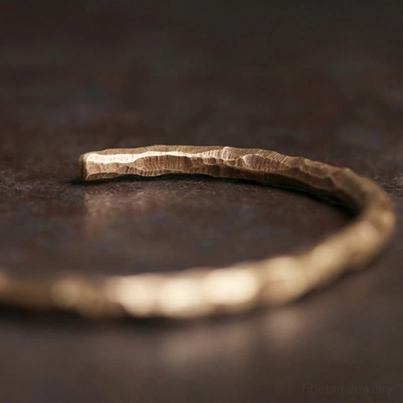 Tibetan hammered brass cuff bracelet side flat lay close-up showing textured surface on dark rustic background