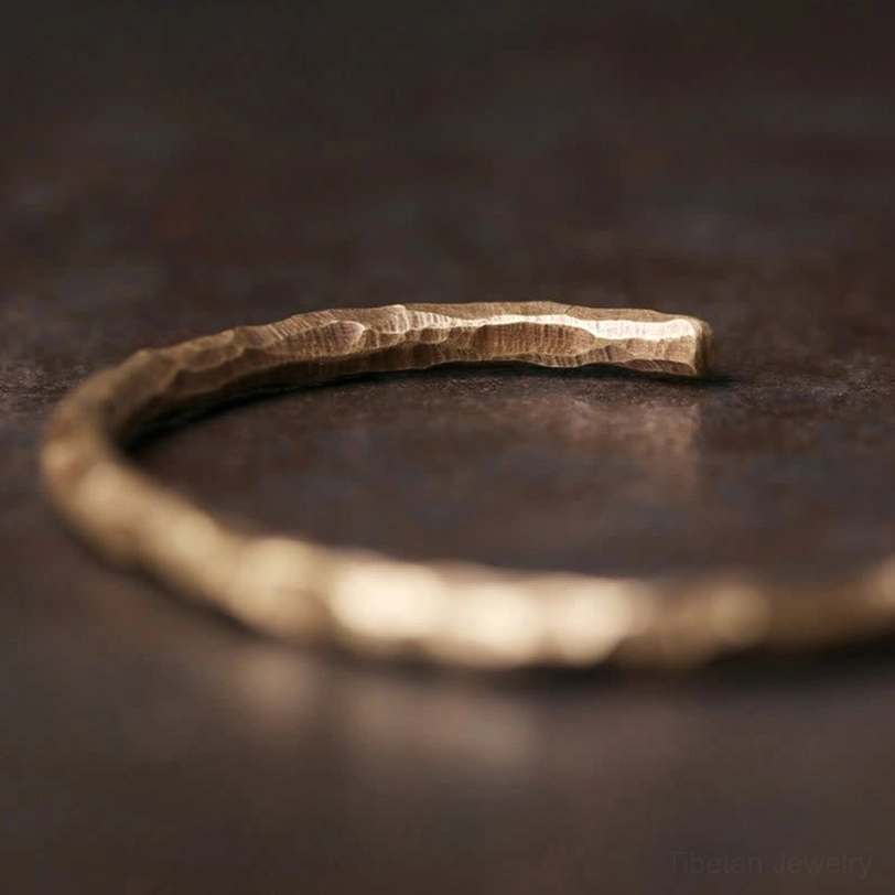 Side flat lay close-up of Tibetan copper cuff bracelet with hand-hammered textured surface on dark background