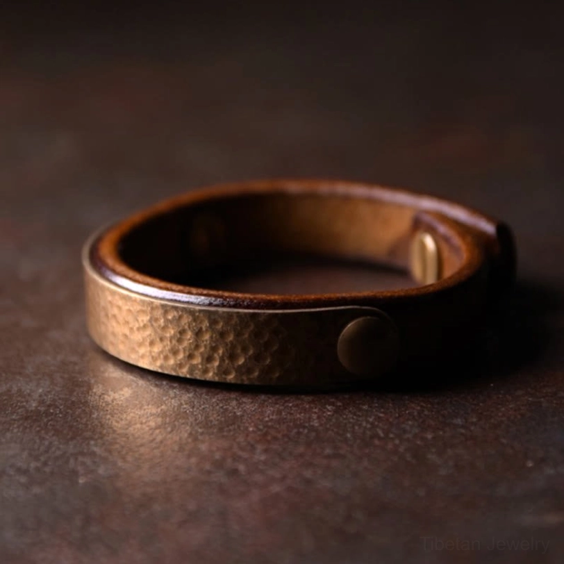 Vintage handmade Tibetan copper brass leather cuff bracelet with textured metal surface and brass rivets on dark background