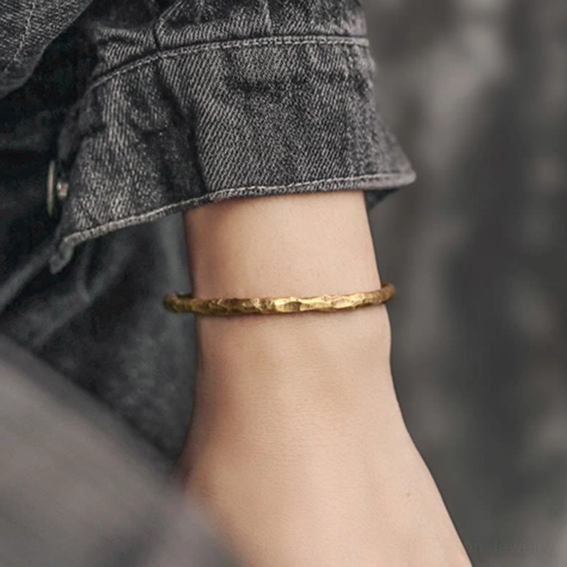 Tibetan hammered copper cuff bracelet worn on human wrist with denim clothing showing textured brass finish
