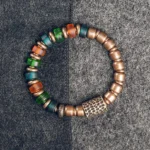Tibetan copper and colorful glass bead prosperity bracelet flat lay, showing mixed vibrant beads with hammered metal accent bead on gray fabric