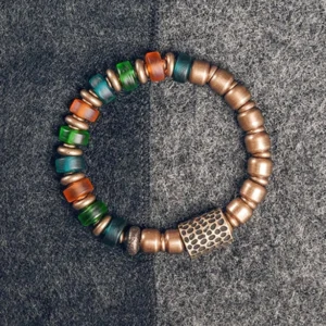 Tibetan copper and colorful glass bead prosperity bracelet flat lay, showing mixed vibrant beads with hammered metal accent bead on gray fabric