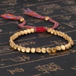 Tibetan copper healing bracelet with matte gold beads and mixed-color woven tassel on dark background