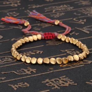 Tibetan copper healing bracelet with matte gold beads and mixed-color woven tassel on dark background