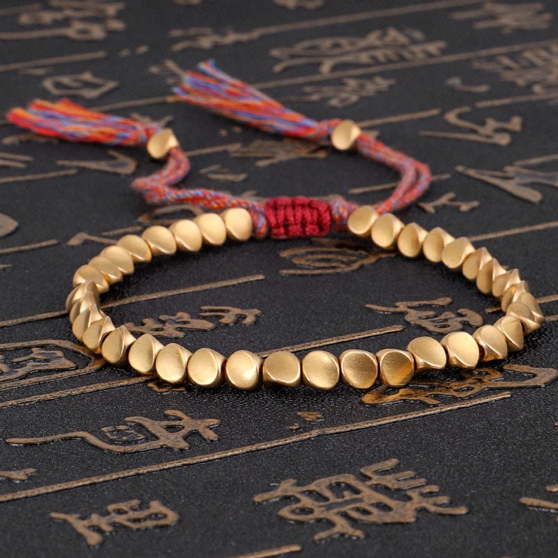 Tibetan copper healing bracelet with matte gold beads and mixed-color woven tassel on dark background