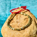 Handmade Tibetan copper beads healing bracelet with red tassel on stone background, flat lay top view