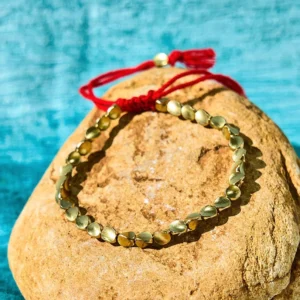 Handmade Tibetan copper beads healing bracelet with red tassel on stone background, flat lay top view