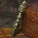 Handmade tibetan copper vajra dorje with detailed carved wrathful deity face on aged bronze finish, displayed on wooden display box with bamboo mat