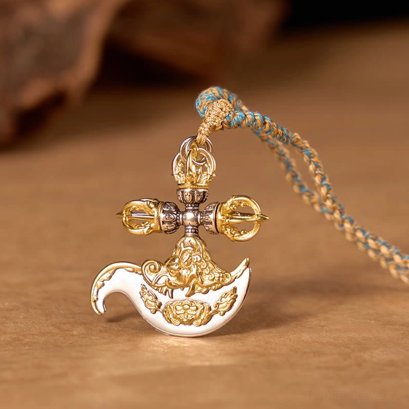 Tibetan copper vajra pendant necklace with dual gold and silver tone, displayed on warm wooden table with blue-brown braided rope showing left three-quarter view and embossed religious relief patterns