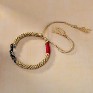 Angled view of Tibetan cotton rope protection bracelet displaying golden braided body with red accent knot and dark twisted decorative detail