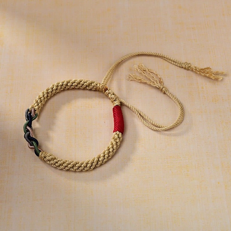 Angled view of Tibetan cotton rope protection bracelet displaying golden braided body with red accent knot and dark twisted decorative detail