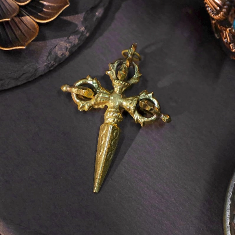 Cross dorje vajra pendant with polished aged brass finish - sharp tapered prongs and ornate ritual carvings close-up view on slate stone