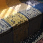 Handwoven Tibetan damask throw blanket with vibrant color blocking and floral motifs displayed on sunlit sofa