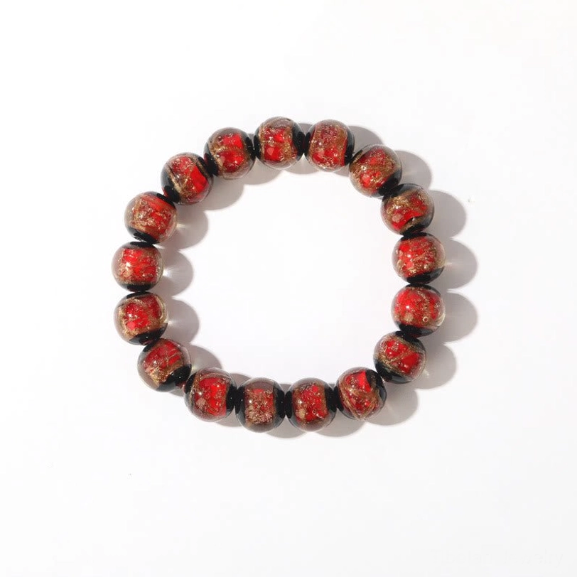 Single dark red-brown Tibetan glass bead bracelet with round glossy minimalist beads displayed in front flat lay on plain wooden desktop