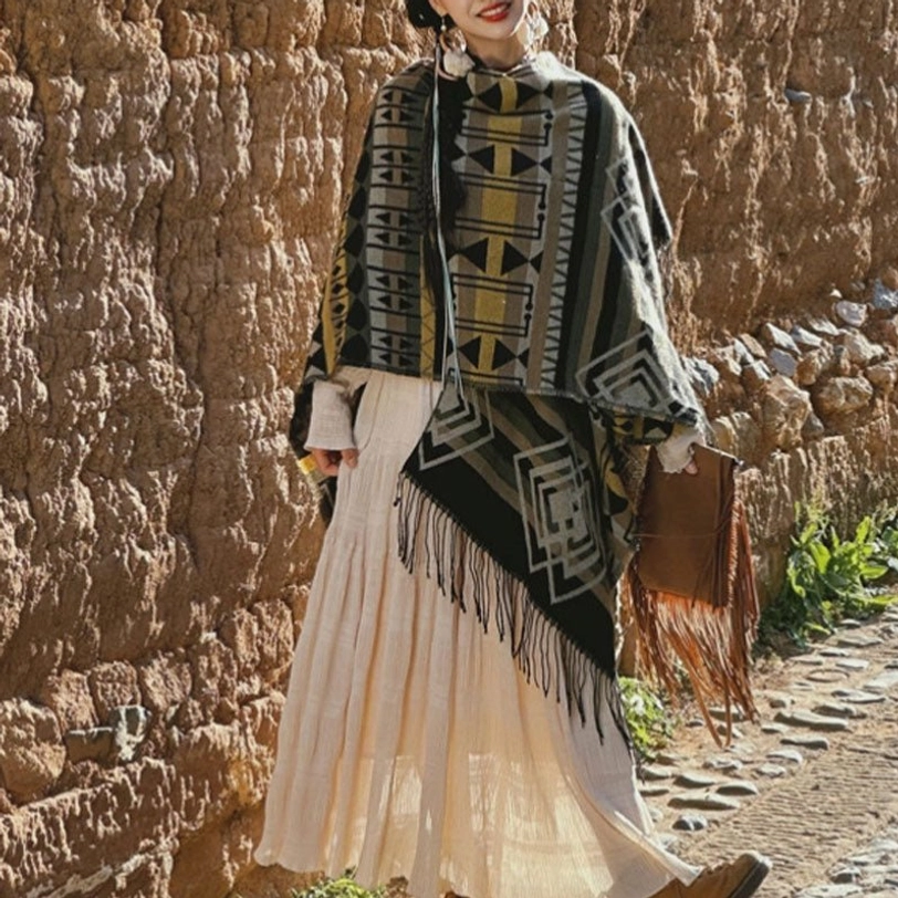 Dark ethnic tassel poncho with tribal geometric prints, paired with fringe handbag, adobe wall alley setting