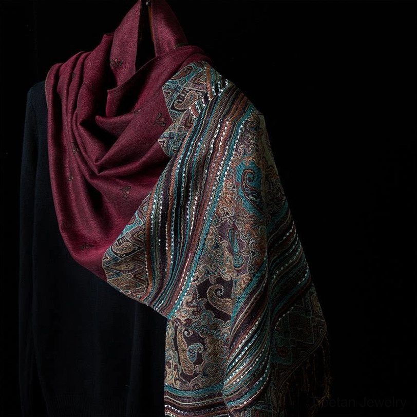 Tibetan dark magenta tassel shawl with geometric patterns in oblique hanging position, showing burgundy solid section and muted patterned weave on black knit prop