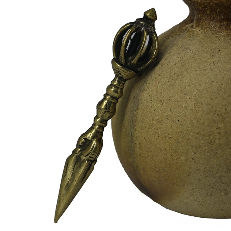 Tibetan ritual dorje tool displayed beside ceramic vessel showing antique dark bronze finish and nine-strand crown configuration