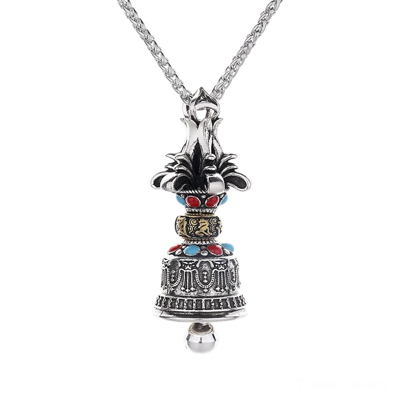 Tibetan Dorje Vajra Bell necklace pendant with red and blue gemstone inlay details, antique silver vintage finish, left front view against kraft paper
