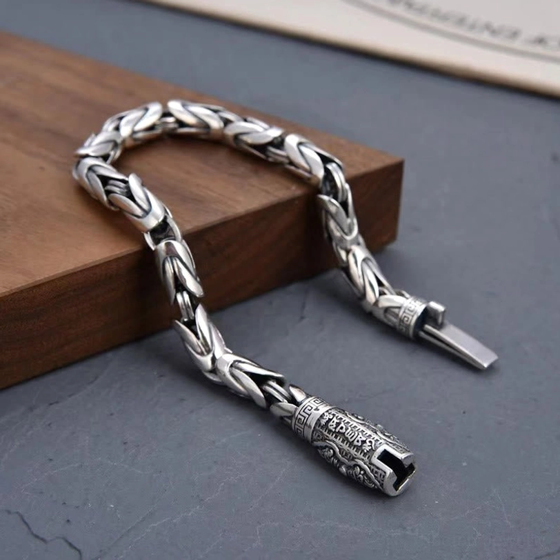 Tibetan Buddhist copper mantra bracelet low angle side view displaying dual engraved metal clasps and antique silver finish on dark tabletop