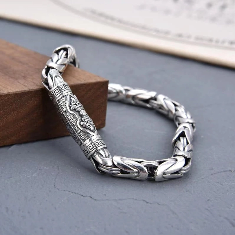Three-quarter angle view of Tibetan Dorje Vajra copper bracelet showing curved braided chain with vintage carved details and wooden block display