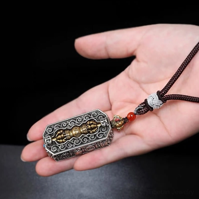 Overhead view of Tibetan vajra pendant with brown braided woven rope and red bead ornament displayed horizontally on black background