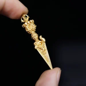 Tibetan Dorje Vajra pendant side view in bright gold tone, held between thumb and index finger against dark background, showing intricate carved relief details